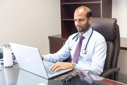 Top Physician in Bayonet Point FL For Cardiovascular Disease Treatment Looking At Patient's Info On His Laptop