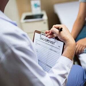 Physician Holding Doctor's Visit Form While Interviewing Bayonet Patient in Her Primary Care Clinic